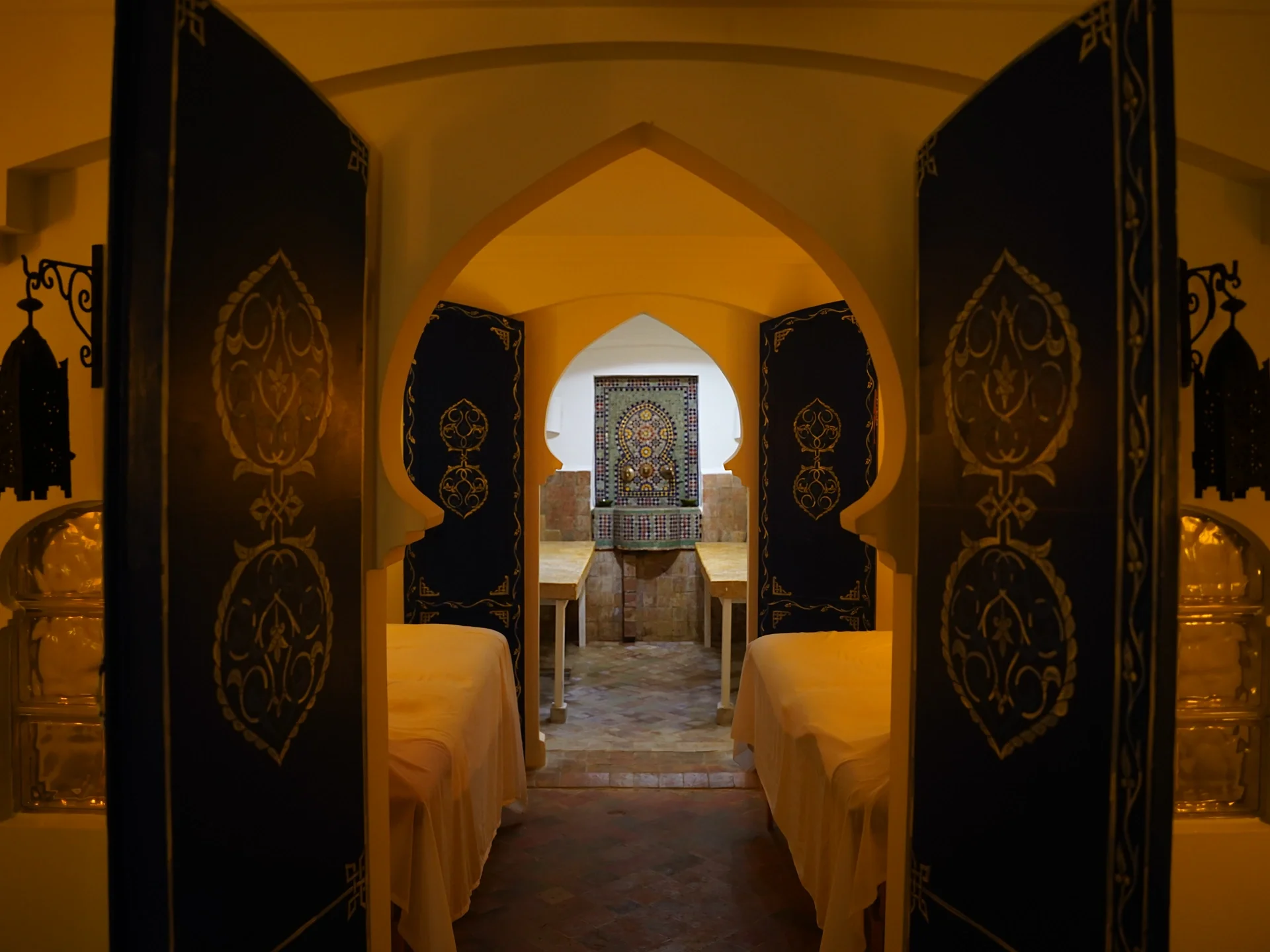 Dos camillas de masaje y puertas abiertas frente a una fuente de azulejos